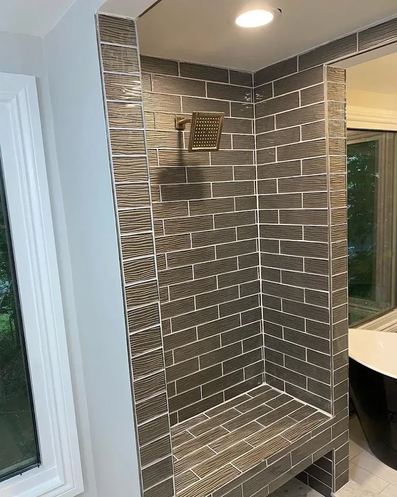 A bathroom with a walk in shower with a bench and a window.