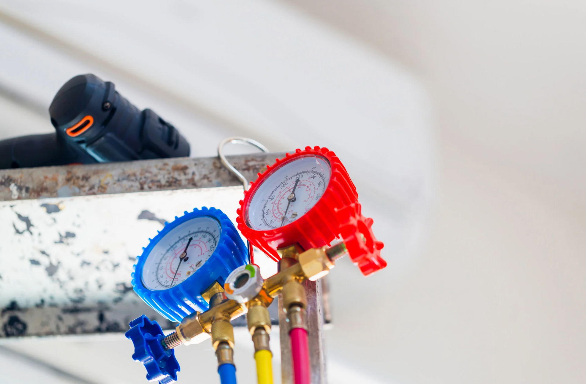 A couple of gauges hanging from a ceiling next to a drill.