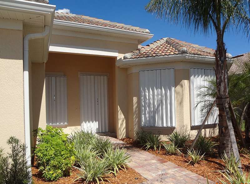 A House With Shutters on the Windows and a Walkway Leading to It — Naples, FL — Wind Safe Shutters LLC