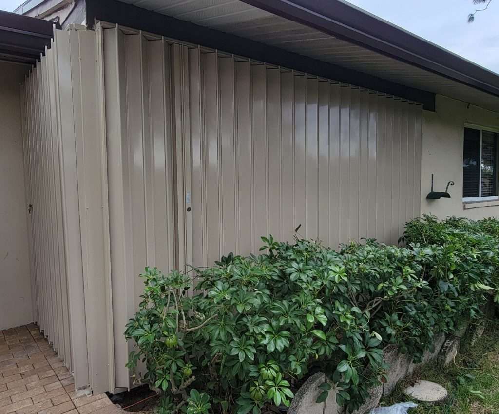 The Side of a House With a Fence and Bushes in Front of It — Naples, FL — Wind Safe Shutters LLC
