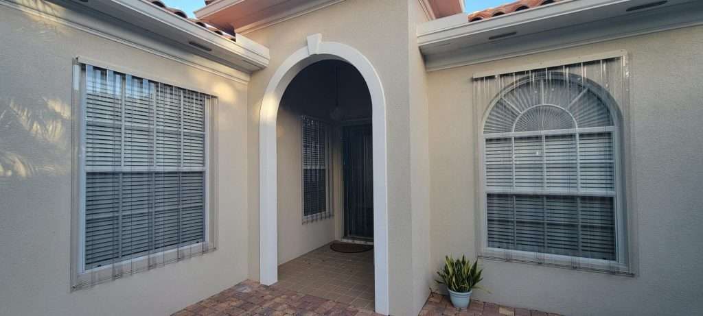 The Front of a House With Arched Windows and a Potted Plant in Front of It — Naples, FL — Wind Safe Shutters LLC