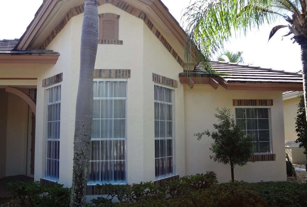 A White House With a Palm Tree in Front of It — Naples, FL — Wind Safe Shutters LLC