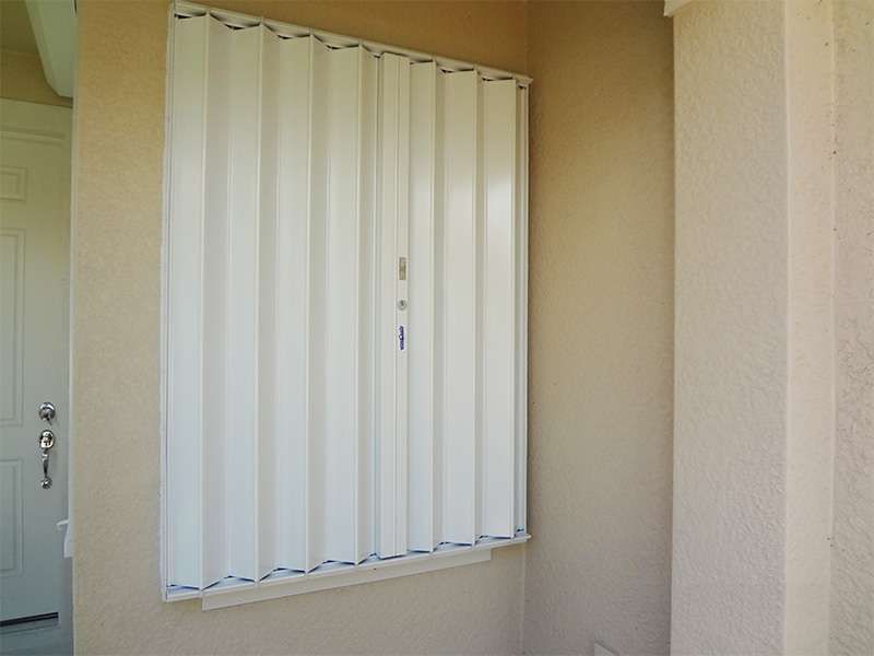 A White Blind Is Hanging on a Wall Next to a Door — Naples, FL — Wind Safe Shutters LLC