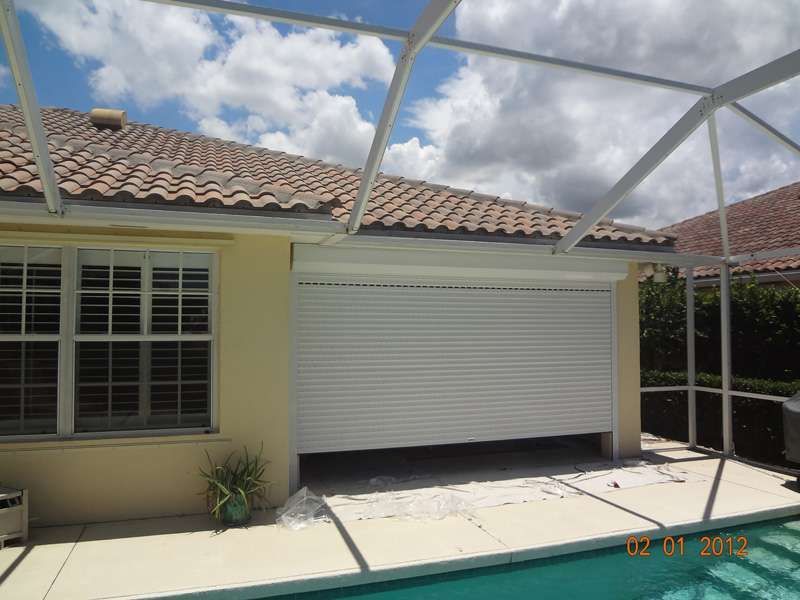 A White Garage Door Is Open Next to a Pool — Naples, FL — Wind Safe Shutters LLC