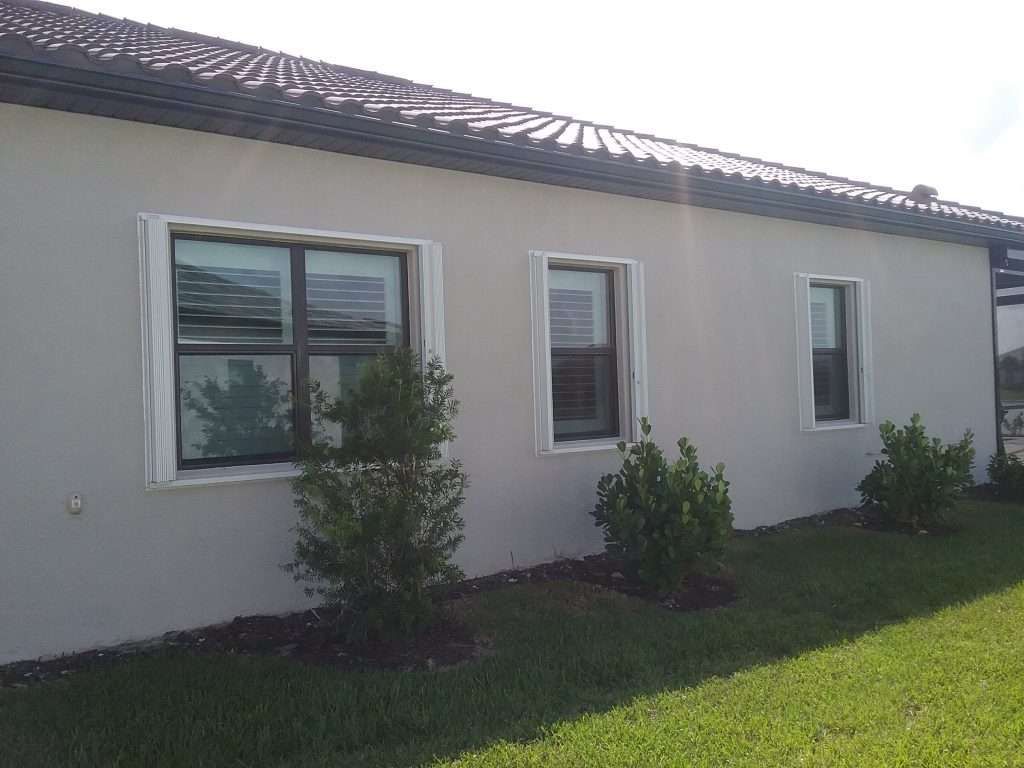 A White House With a Lot of Windows and Bushes in Front of It — Naples, FL — Wind Safe Shutters LLC