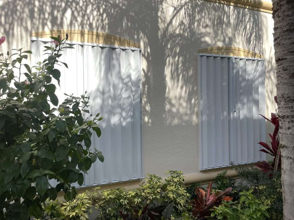 A White Building With Shutters on the Windows and a Tree in the Background — Naples, FL — Wind Safe Shutters LLC