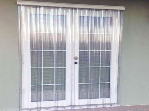 A Pair of Sliding Glass Doors With Clear Curtains on Them — Naples, FL — Wind Safe Shutters LLC