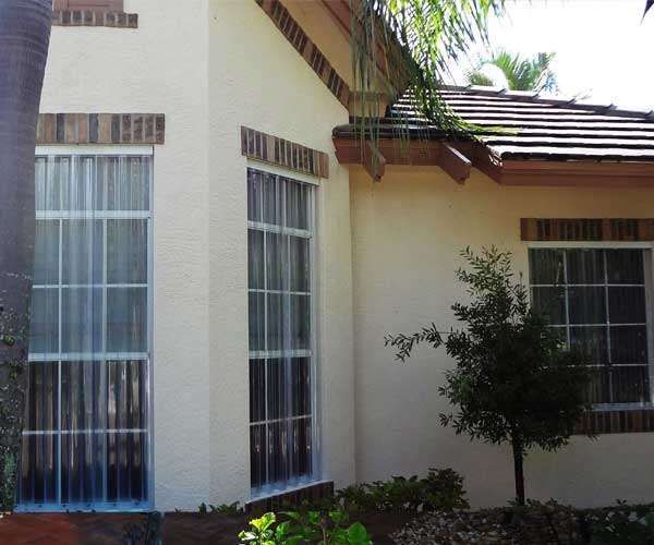 A White House With a Lot of Windows and a Palm Tree in Front of It — Naples, FL — Wind Safe Shutters LLC