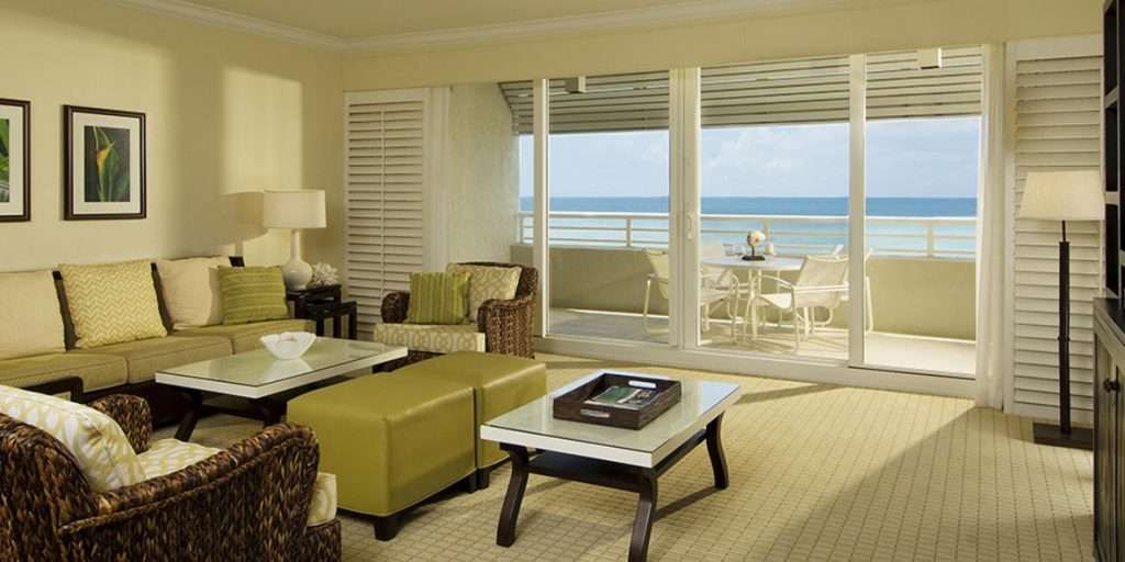A Living Room With a Couch, Table and Sliding Glass Doors Leading to a Balcony — Naples, FL — Wind Safe Shutters LLC
