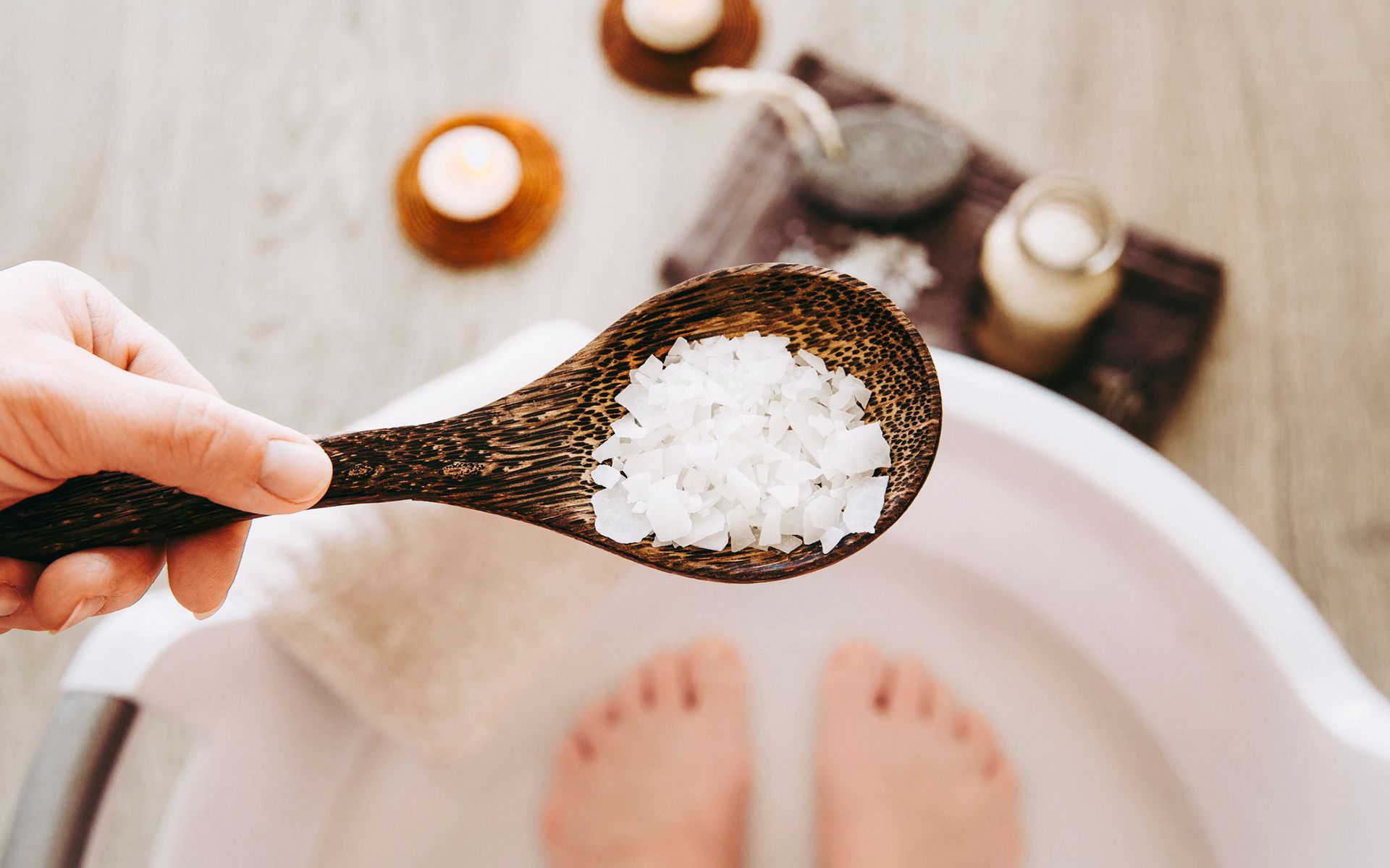 A person is holding a wooden spoon with sea salt in it.