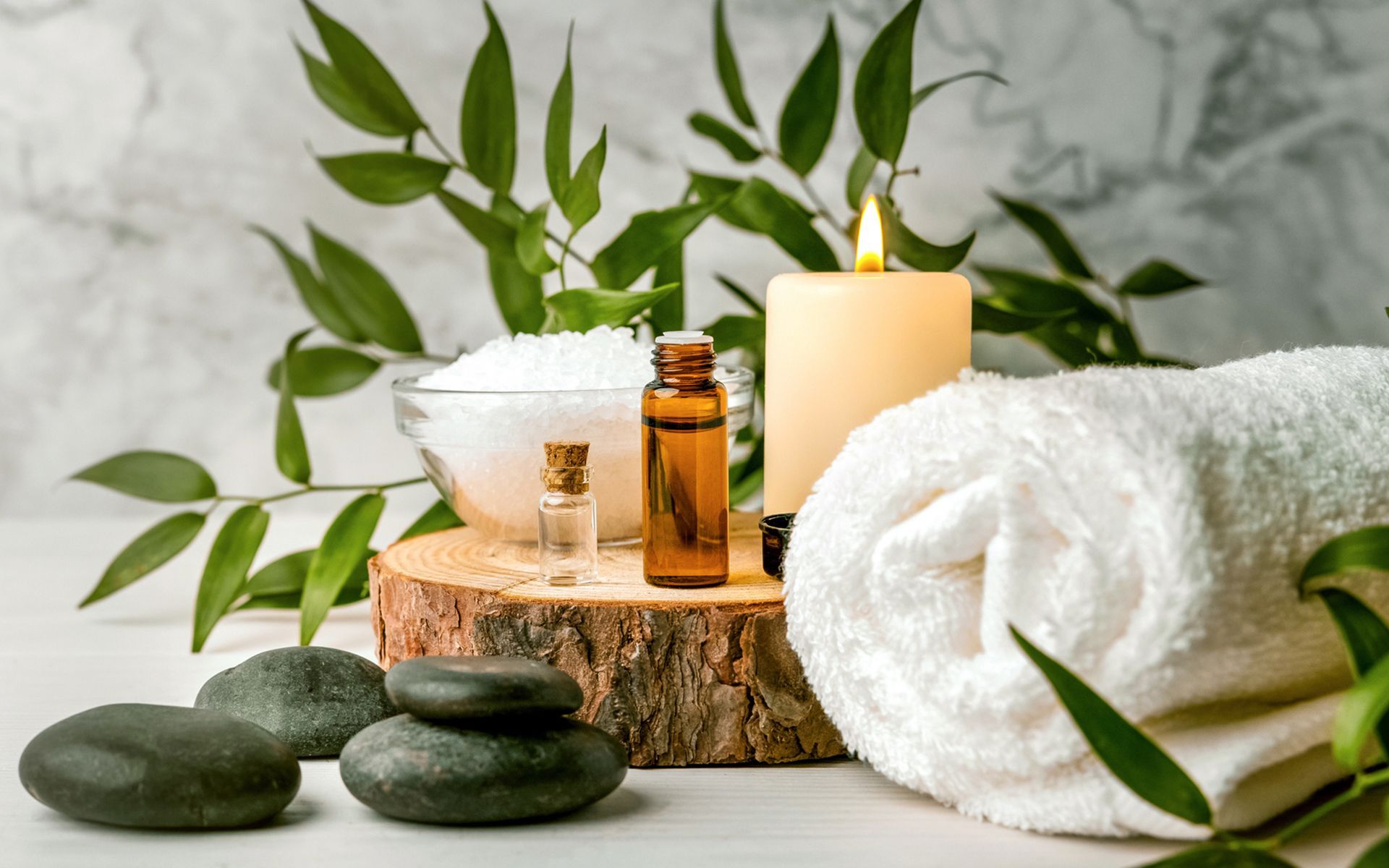A towel , candle , bottles of essential oil and rocks on a wooden stump.