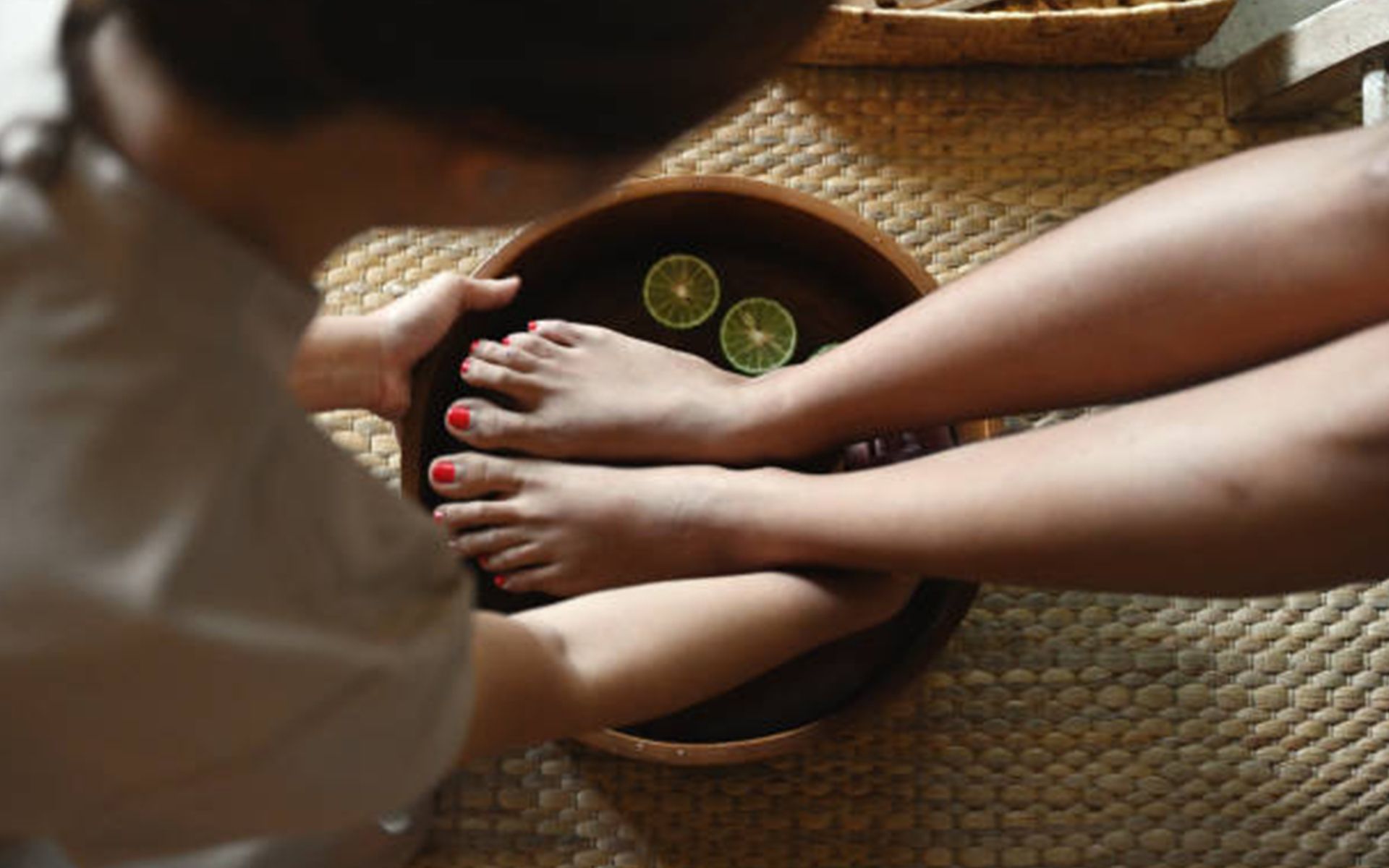 A woman is getting her feet washed in a bowl of water with limes.