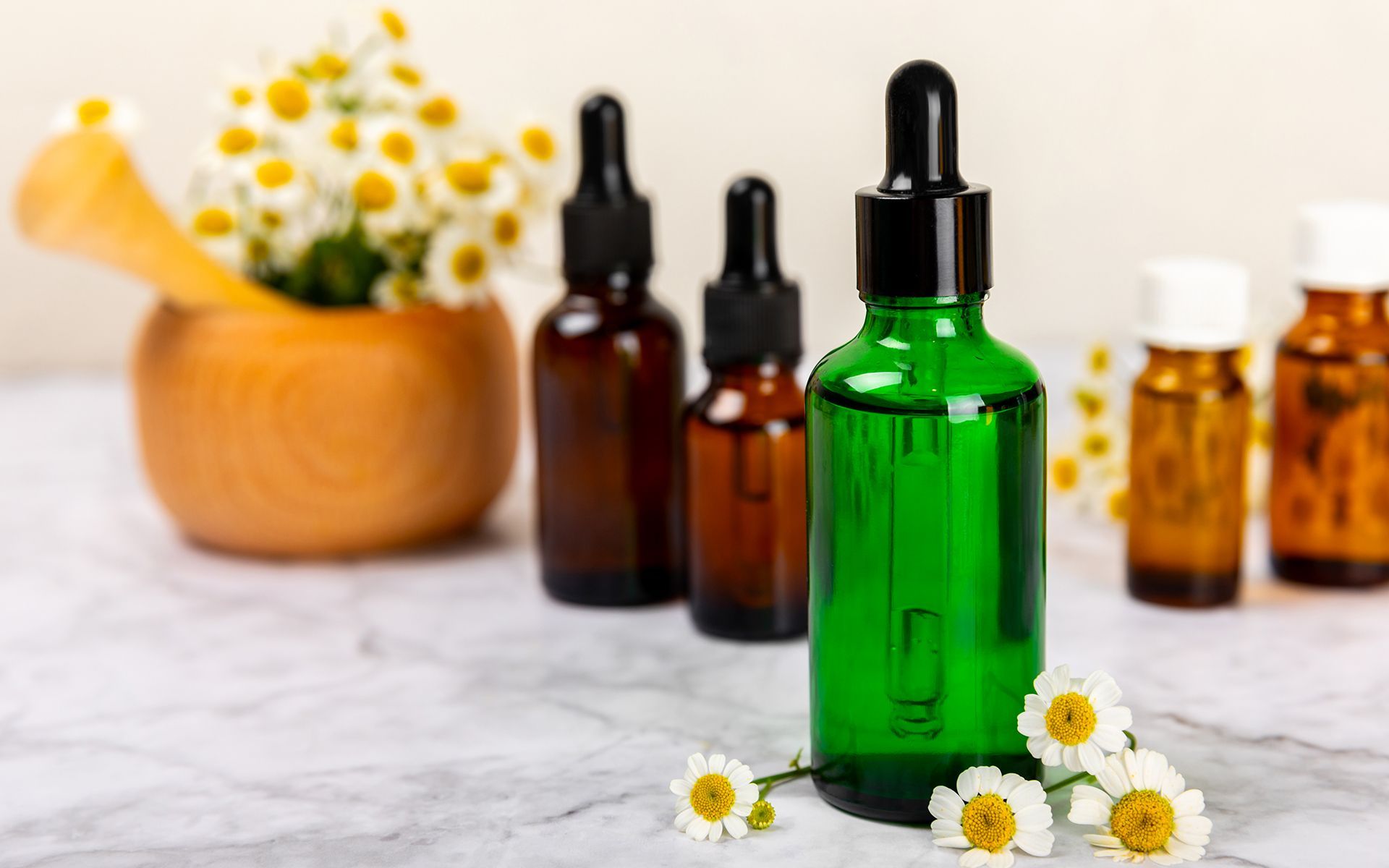 A green bottle with a dropper is sitting on a table next to a mortar and pestle.