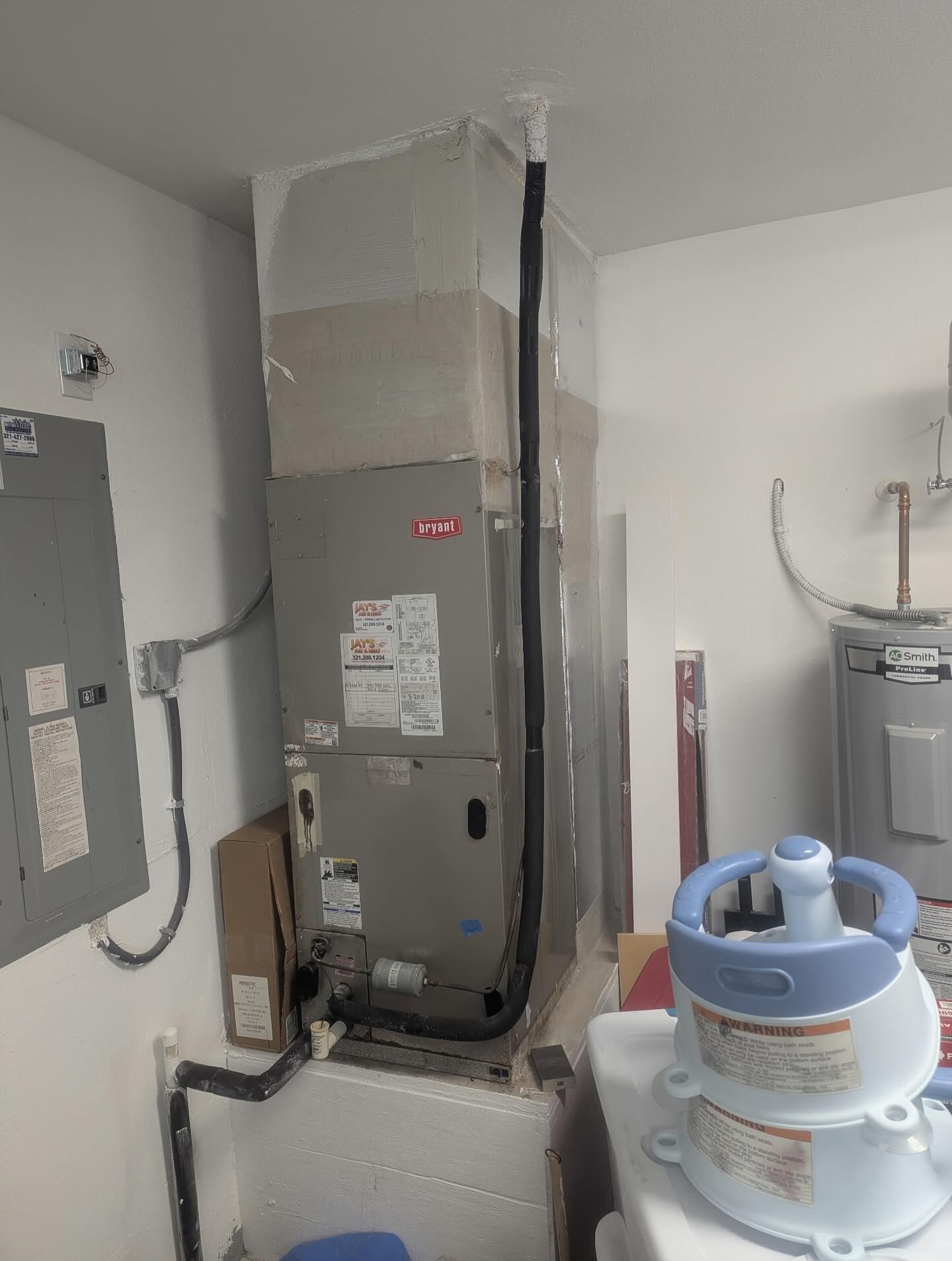 HVAC unit in a utility room; gray metal, tall rectangular shape. Electrical panel and water heater visible.