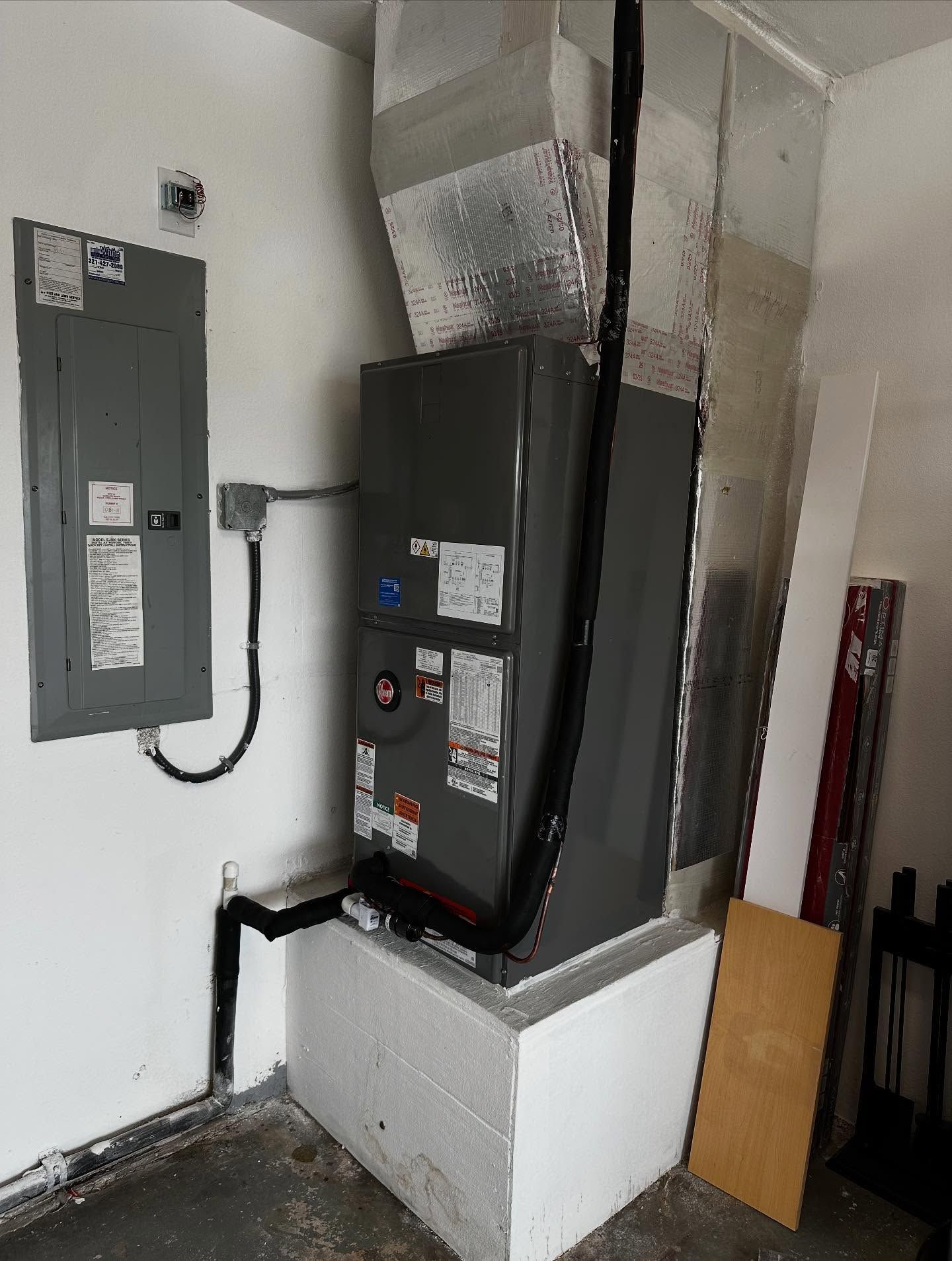 Furnace and electrical panel in a white-walled room. Ductwork, black pipes, and a rectangular, concrete-like base.