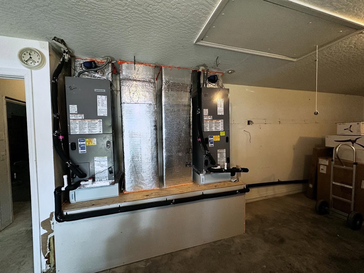 HVAC units mounted on a platform in a utility room. Ductwork, walls, and ceiling present.