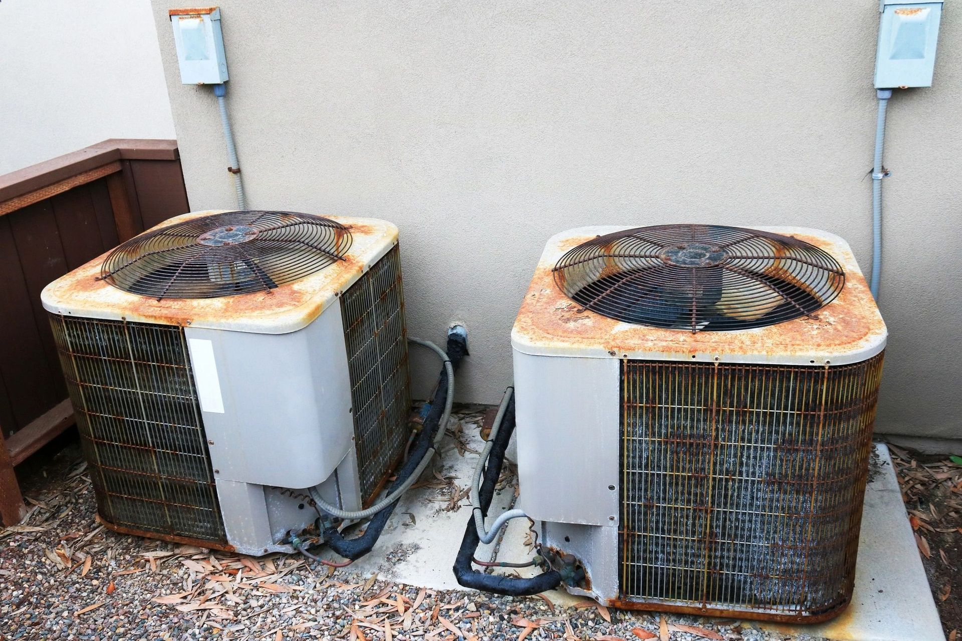 Two rusty air conditioning units sitting on a concrete pad next to a wall.