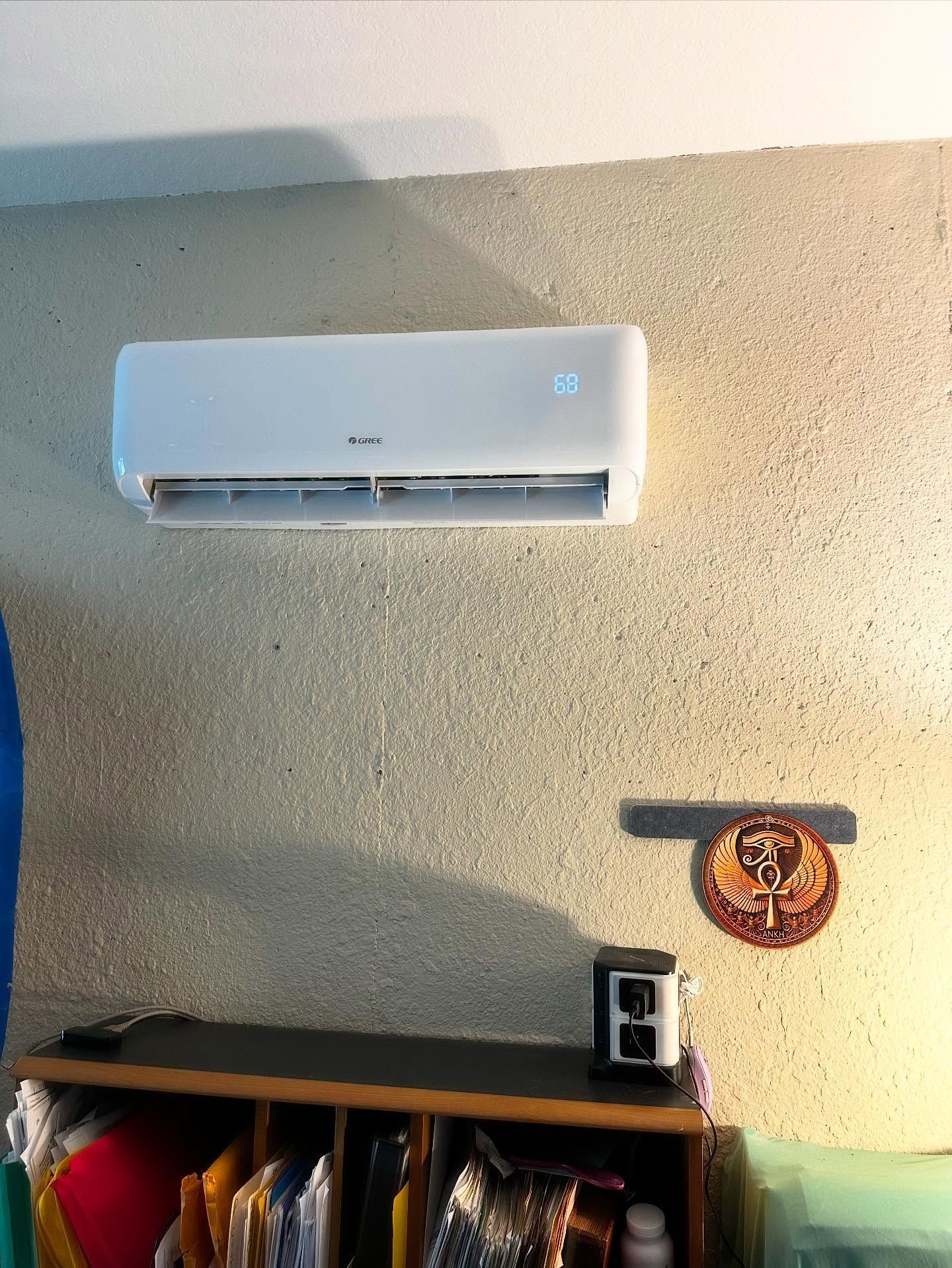 White air conditioner on textured wall, below a wooden shelf with items.