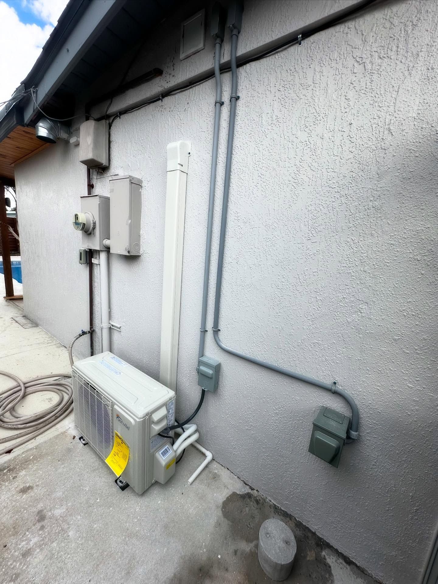 Exterior of a stucco building with electrical conduits, junction boxes, and an air conditioning unit.