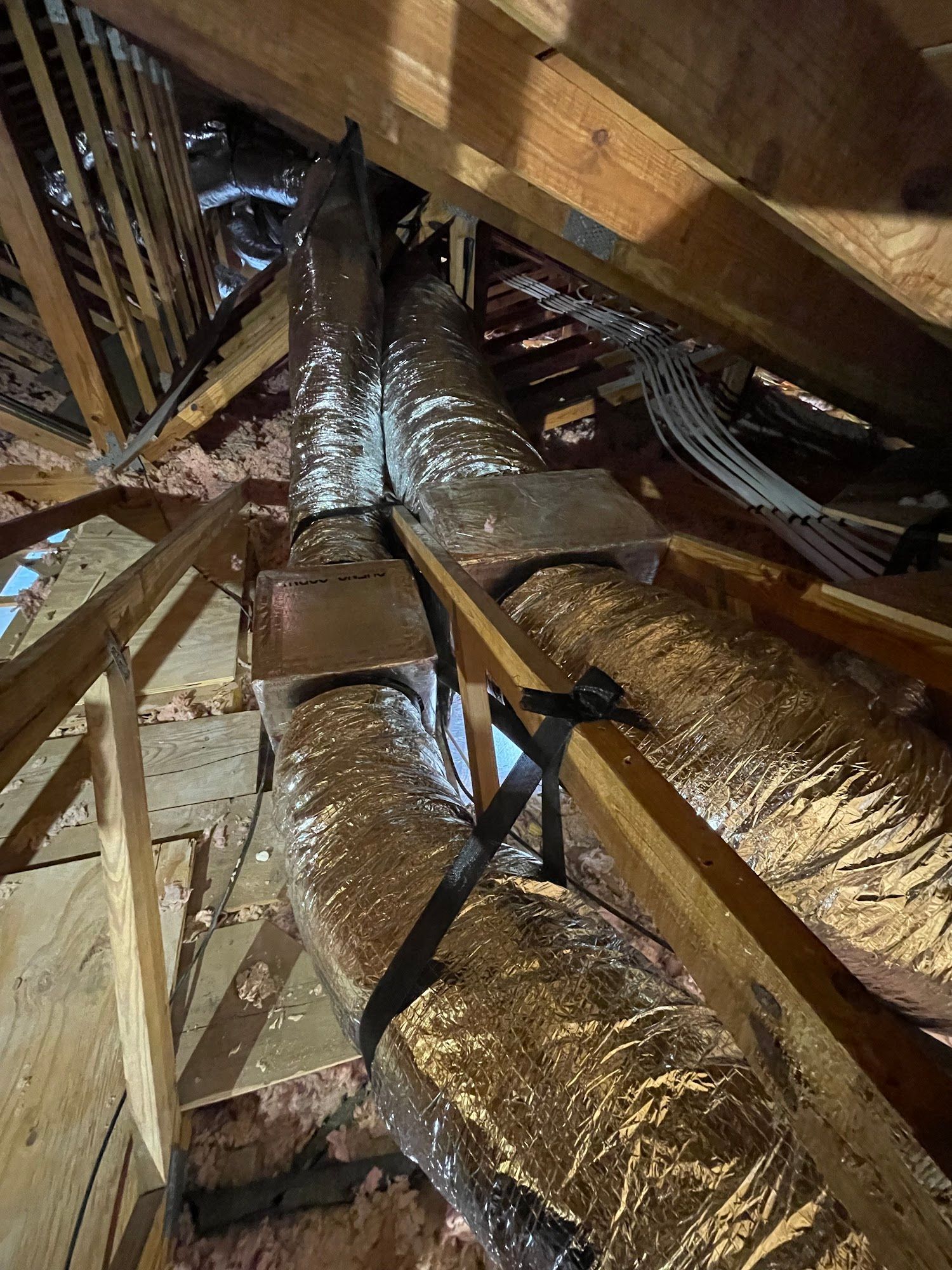 Two insulated HVAC ducts run vertically through an attic, supported by wooden beams.
