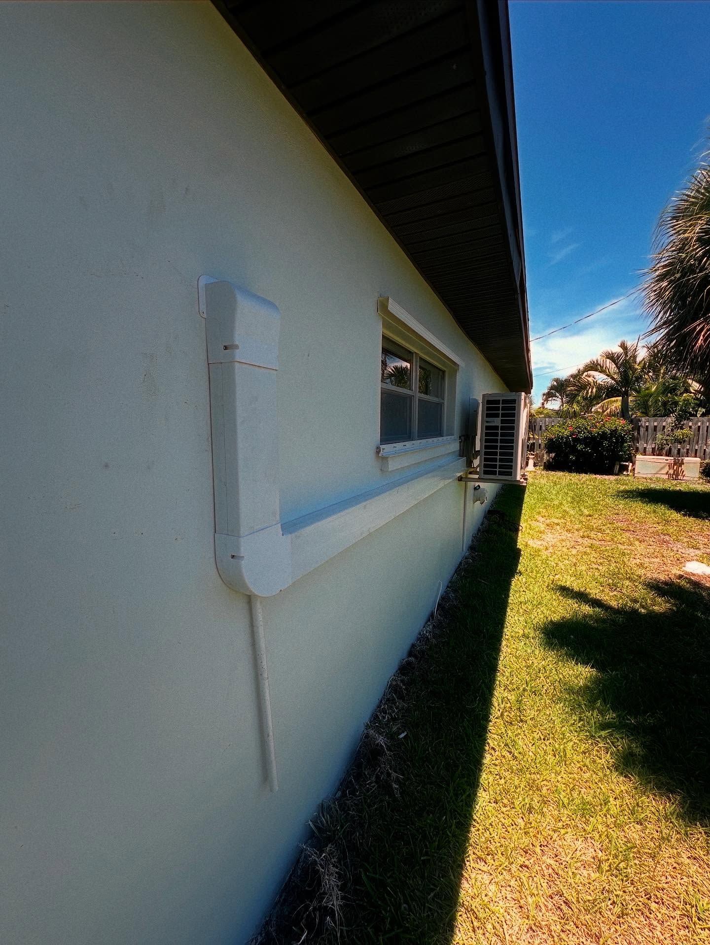 White house exterior with window, gutter, and downspout on a sunny day.