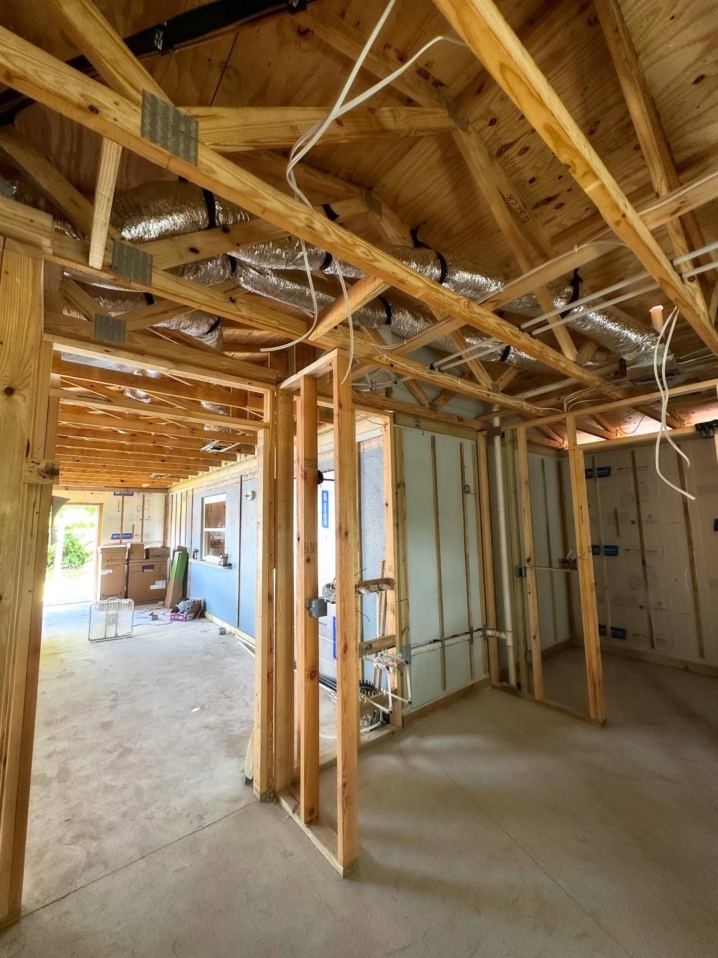 Interior view of a building under construction, showing exposed wooden frame, insulation, and concrete floor.