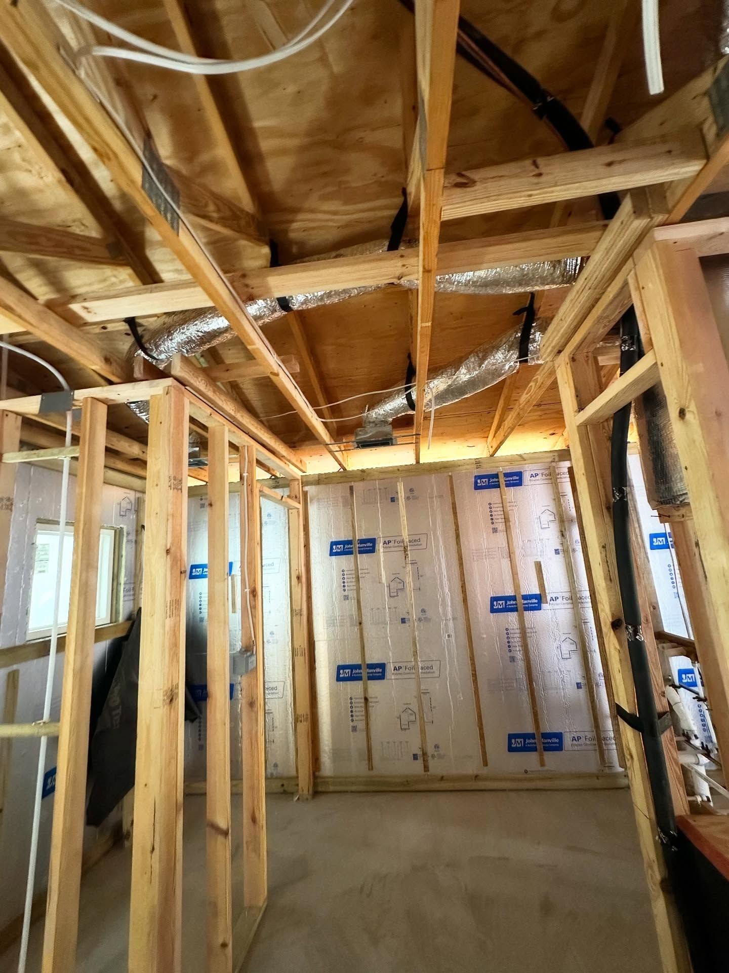 Interior view of a room under construction with exposed wooden beams, insulation, and framing.