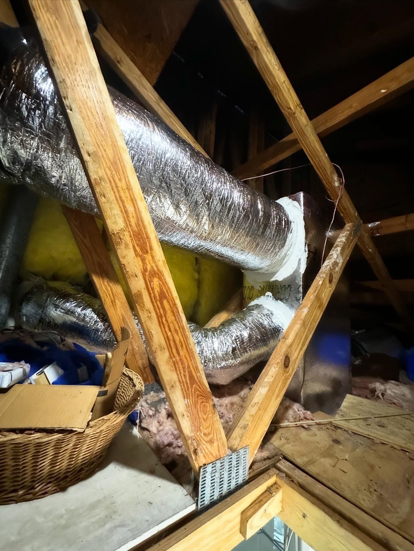 Attic interior with exposed ductwork, wooden beams, and insulation.