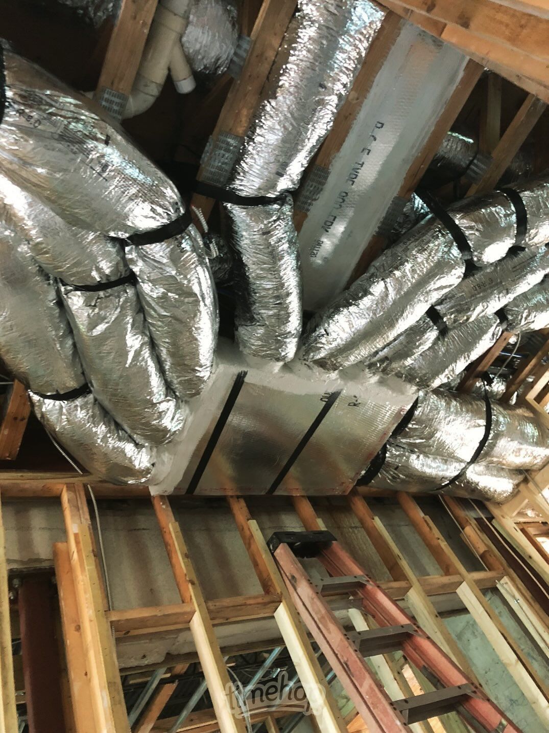 HVAC ductwork in a wood-framed attic space, wrapped in silver insulation, secured with black straps.