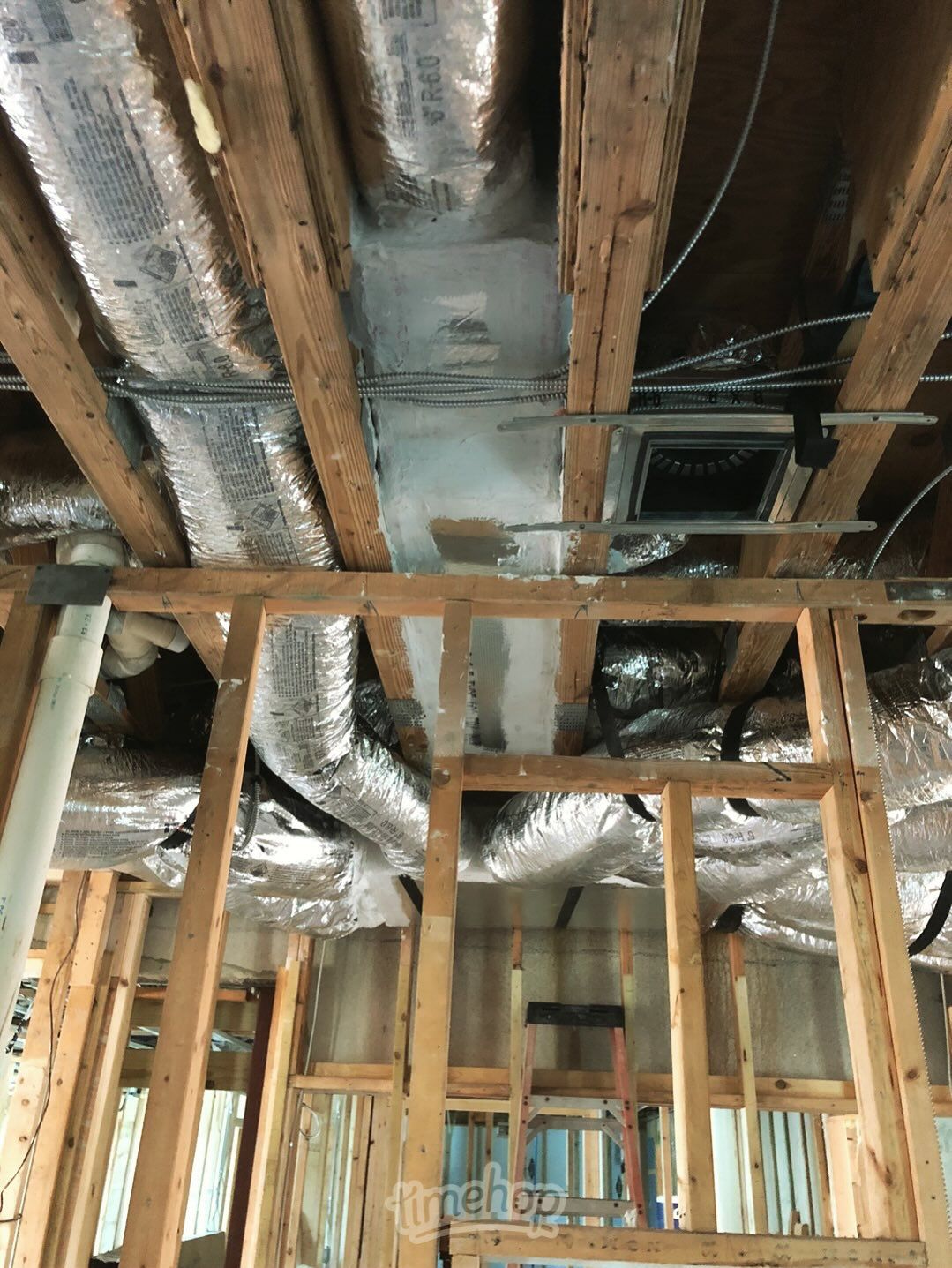 Unfinished construction interior with exposed wooden framing and ductwork wrapped in foil insulation.