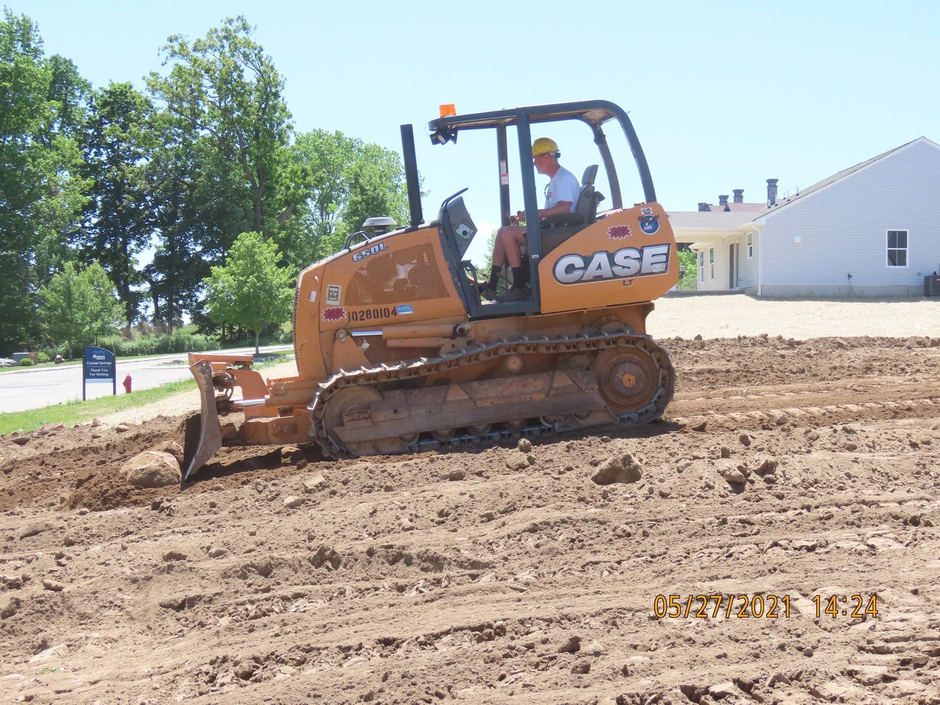 A Case bulldozer levels dirt with a worker in the cab. Outdoors, a sunny day, brown soil.