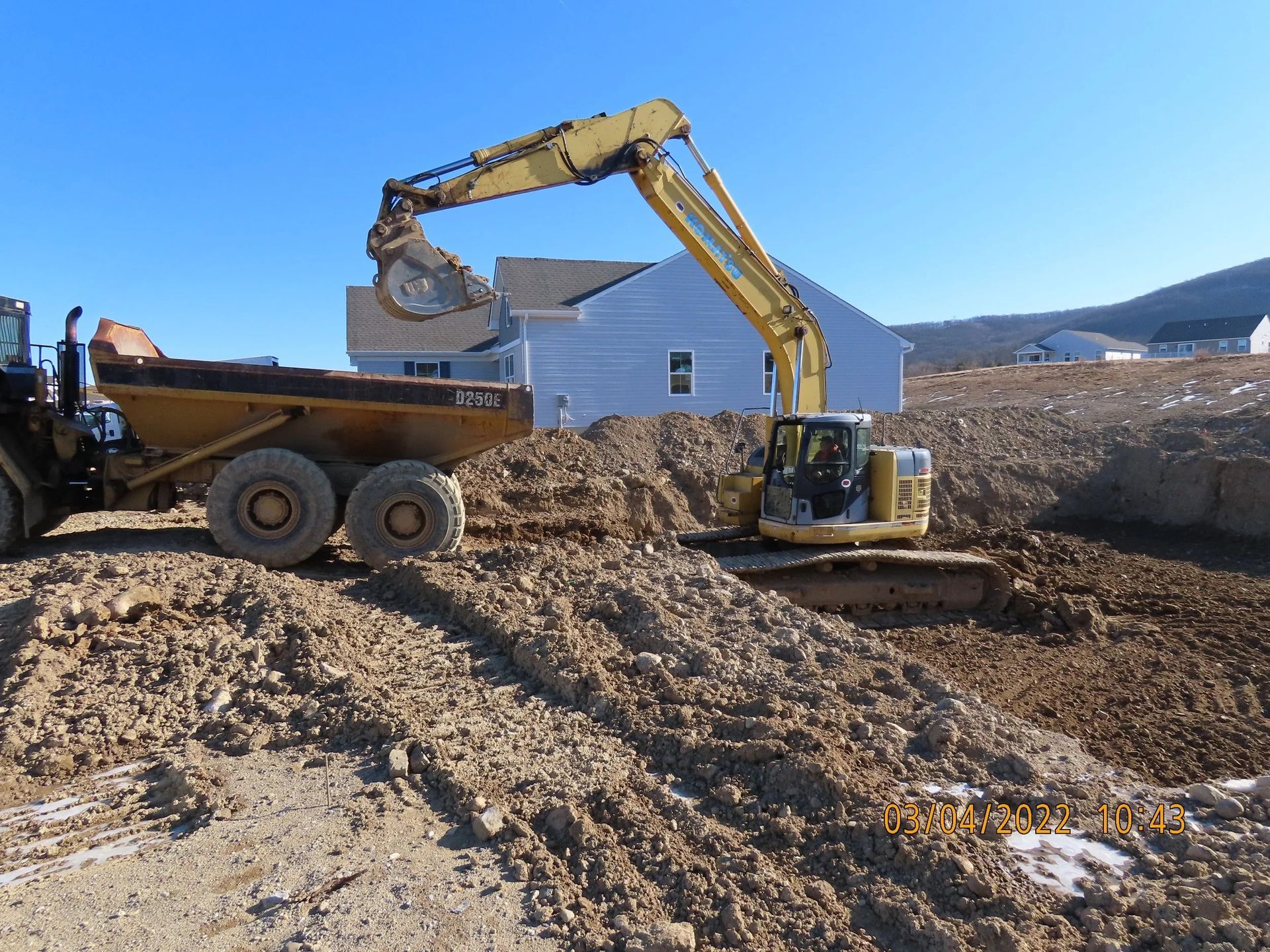Yellow excavator loading a dump truck with dirt at a construction site on a sunny day.
