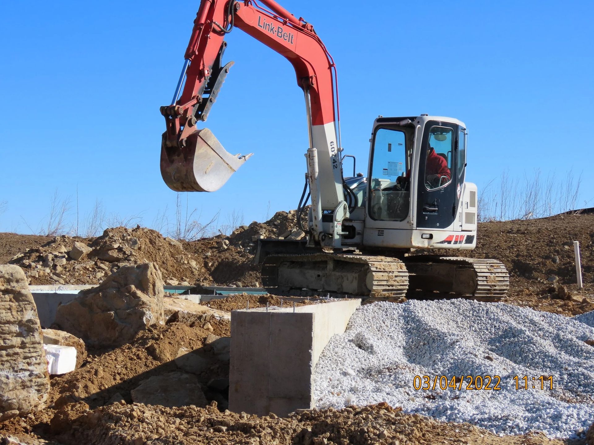 An excavator scoops dirt from a construction site with blue sky in the background.