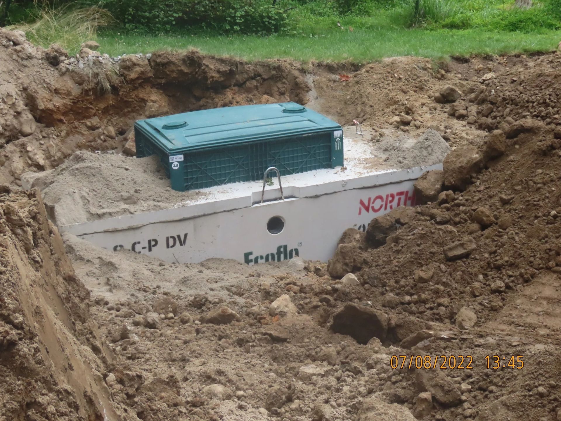 Septic tank in a hole, partially buried with a green lid and concrete wall.