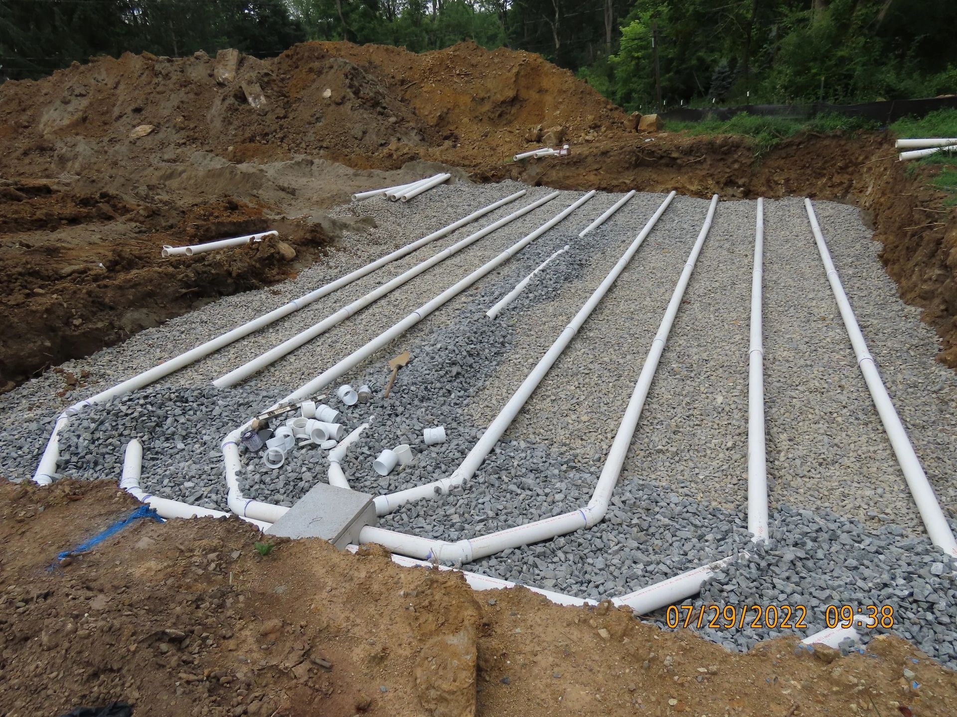 White pipes in gravel bed, part of a drain field construction in a dirt excavation site.