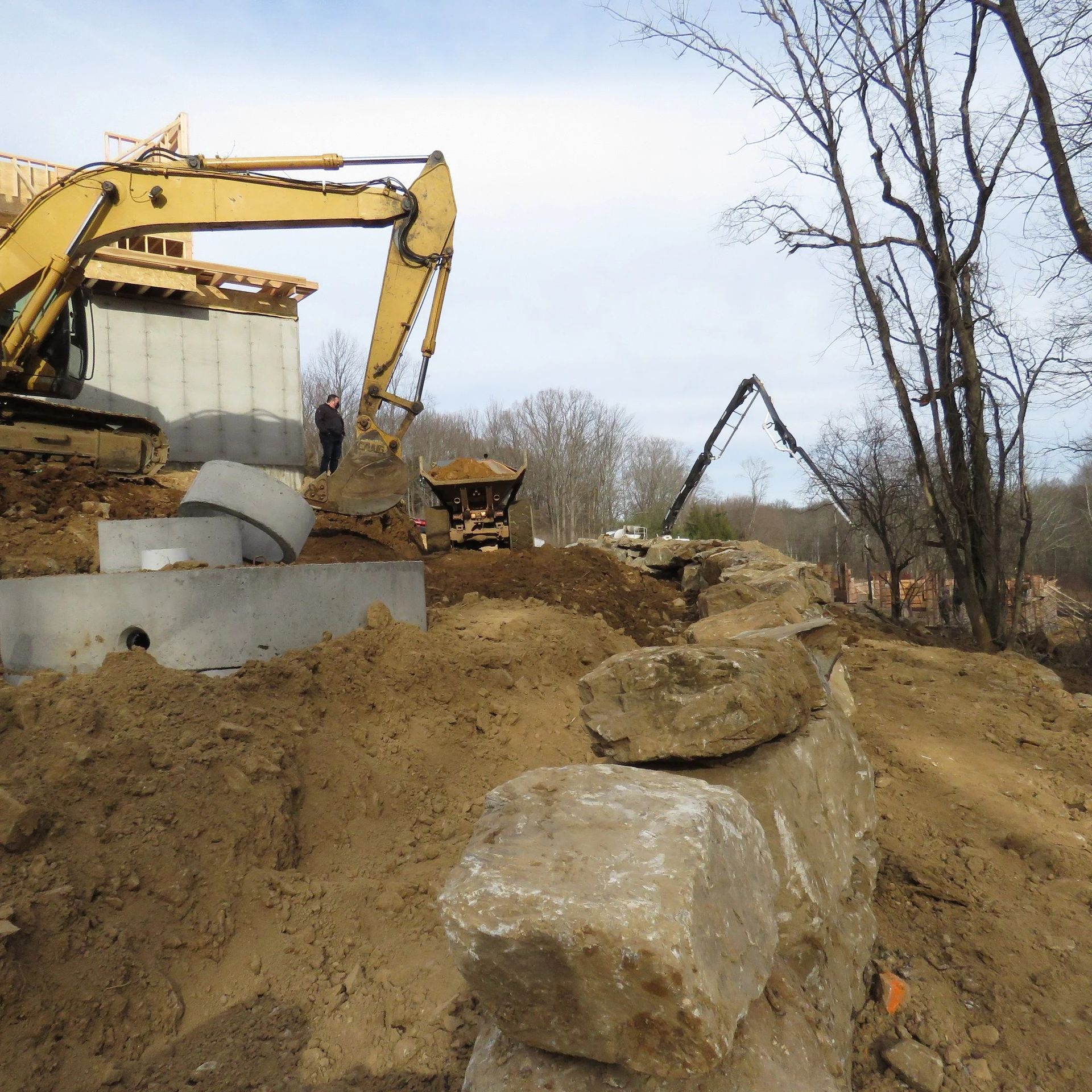 Construction site: Excavator working near concrete foundation, stone wall, and concrete pump boom.