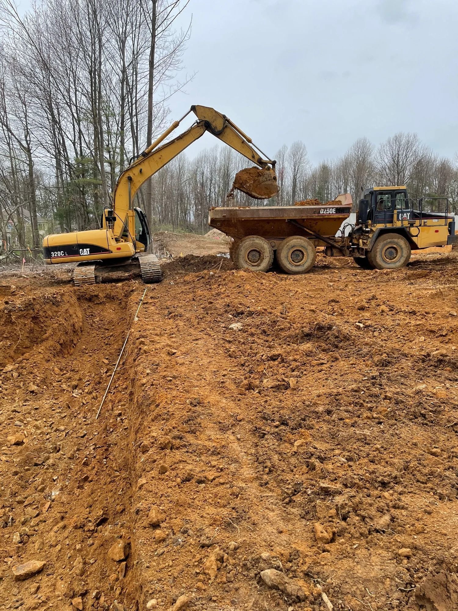 Yellow excavator loading brown earth into a yellow dump truck, construction site.