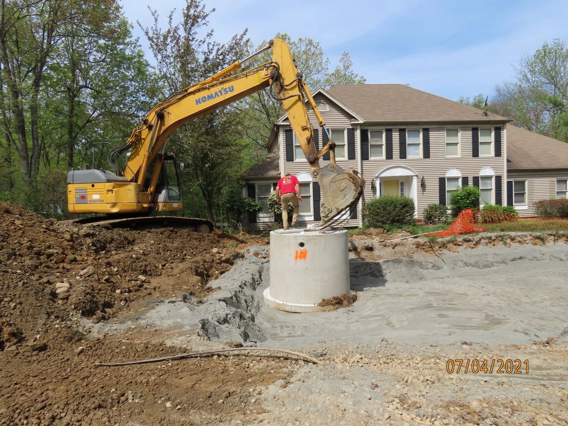 Yellow excavator working near a concrete well, next to a two-story house; construction site.
