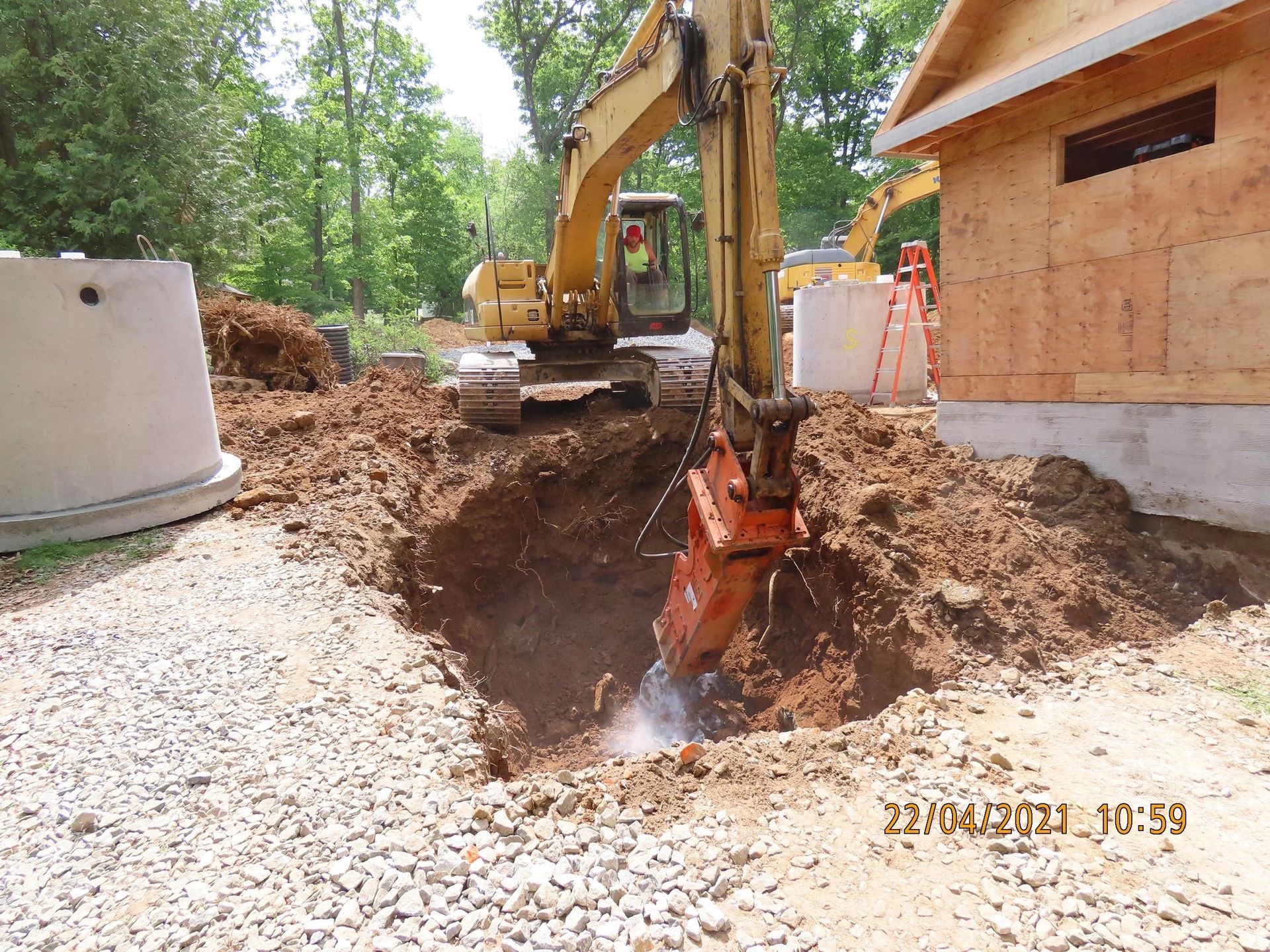 Yellow excavator digging a hole near a small building.