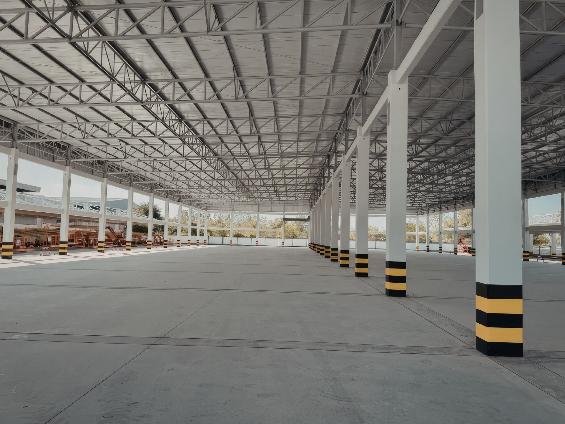 Empty warehouse interior with concrete floor, metal roof, and white columns with yellow and black stripes.