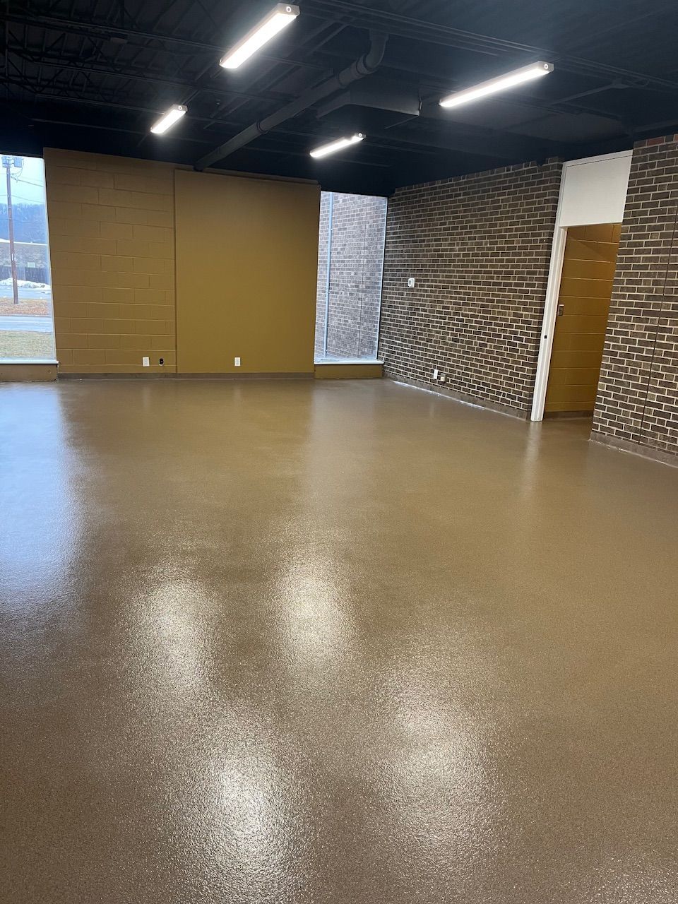 A large empty room with a brown floor and a brick wall.