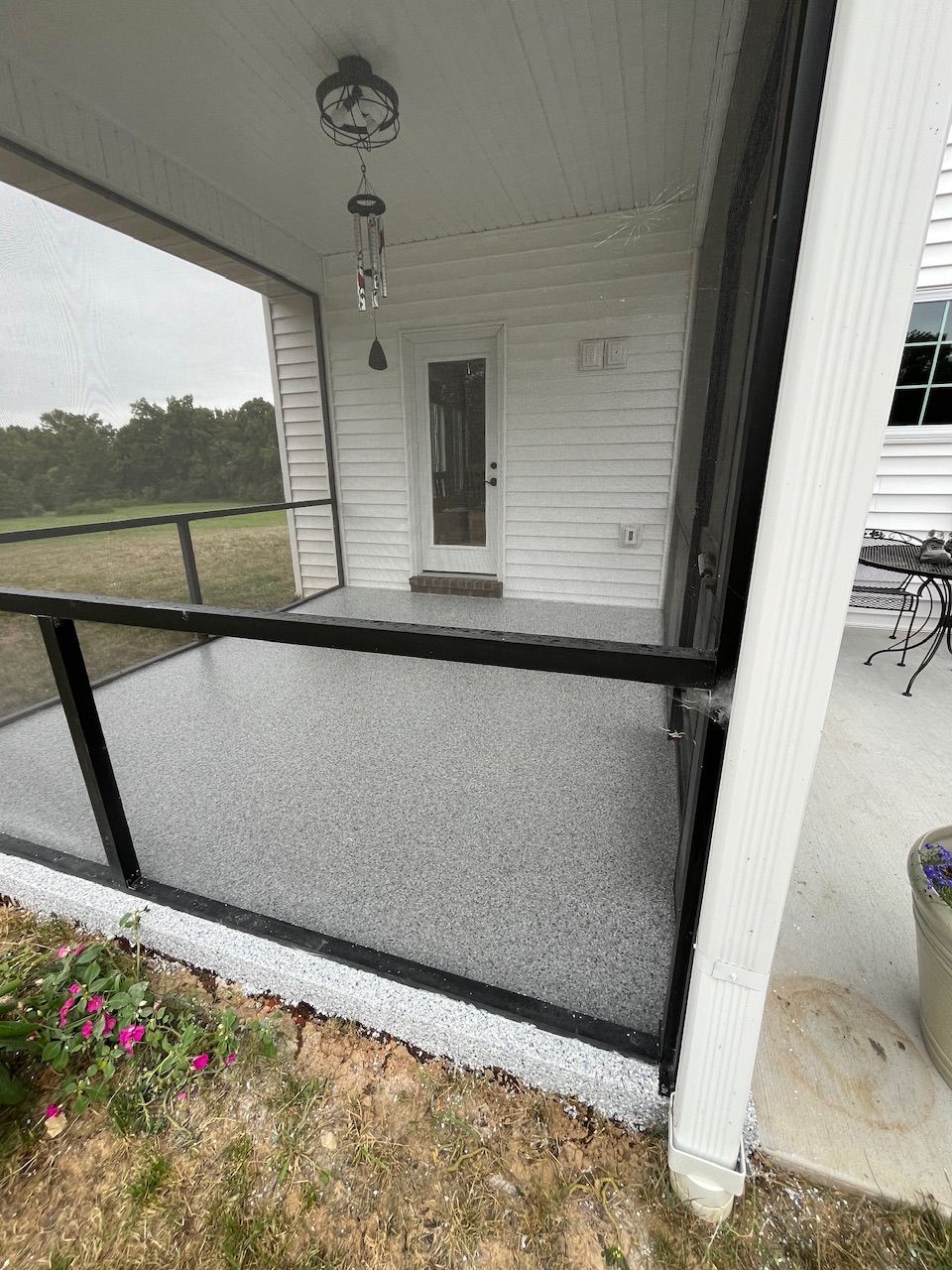 A screened in porch with a black fence and a white house in the background.