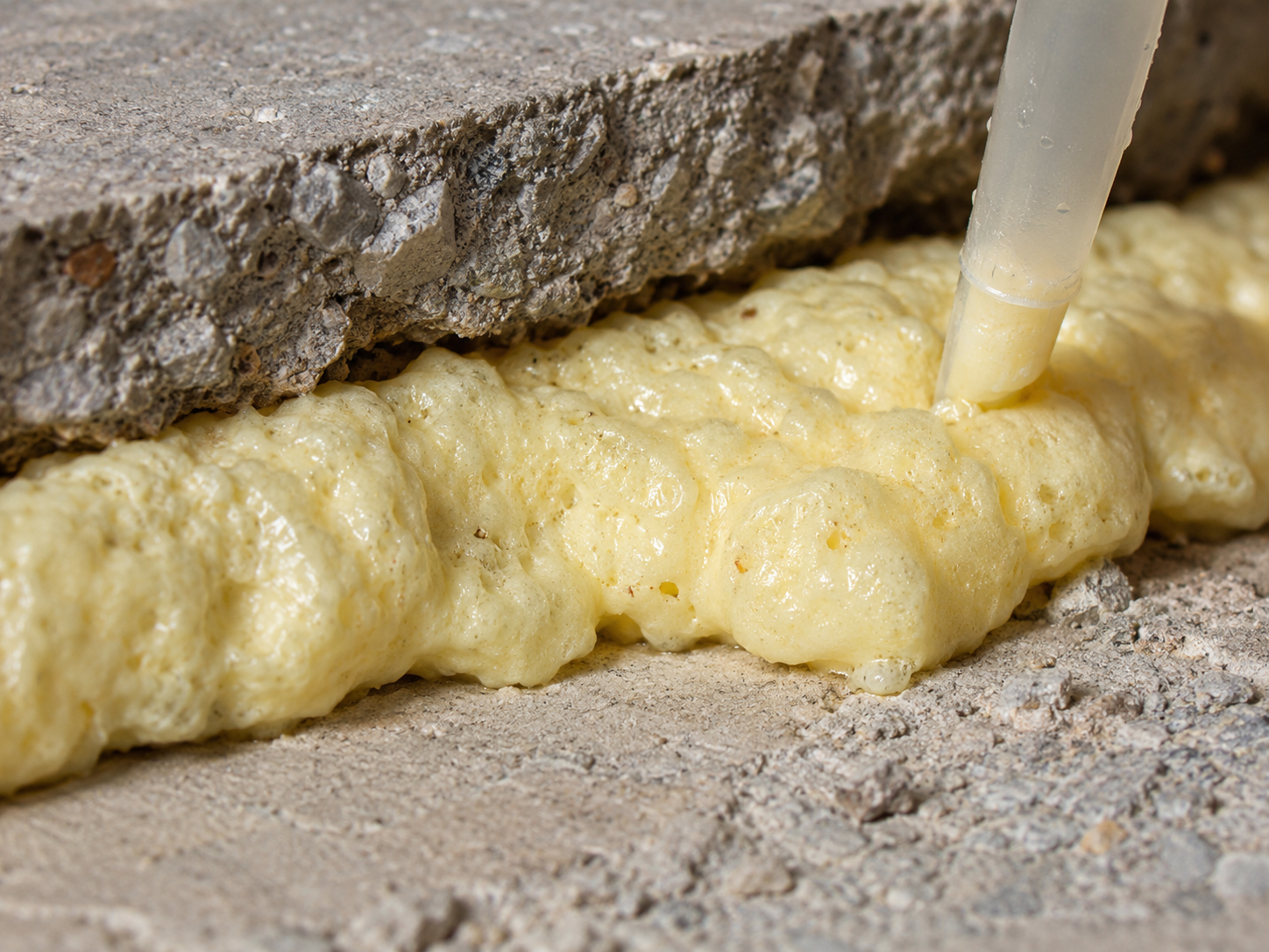 Close-up of expanding polyurethane spray foam filling a gap under a concrete slab.