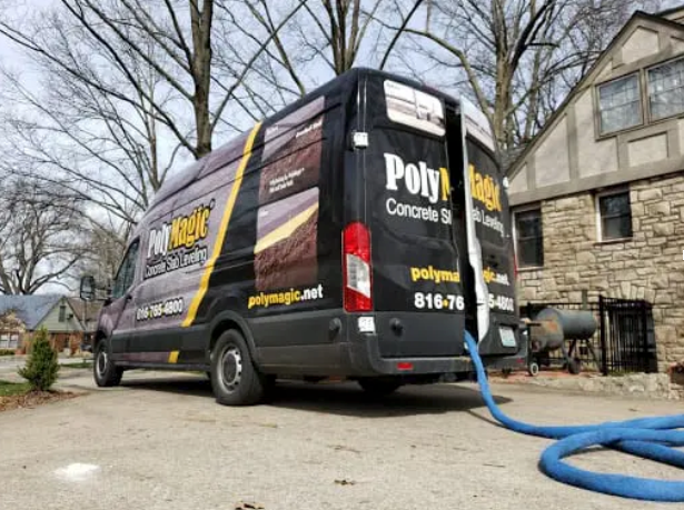 A black van is parked in front of a house with a hose attached to it.