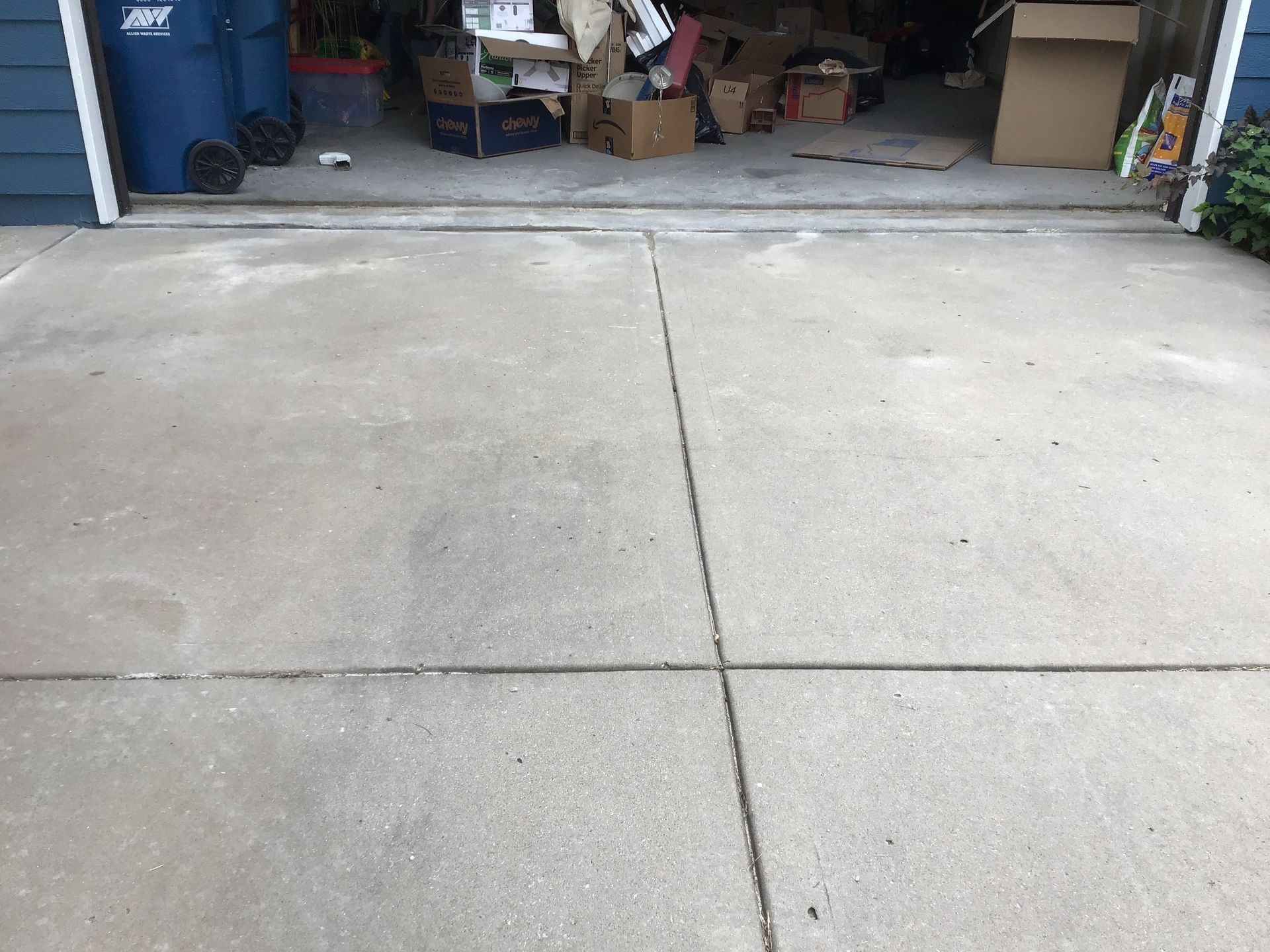 A concrete driveway in front of a garage filled with boxes and trash cans.