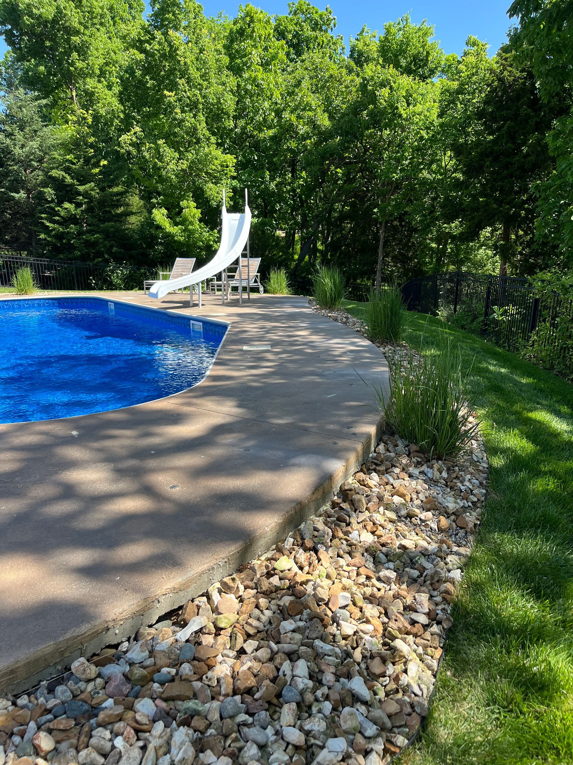 A swimming pool with a slide in the backyard surrounded by trees.