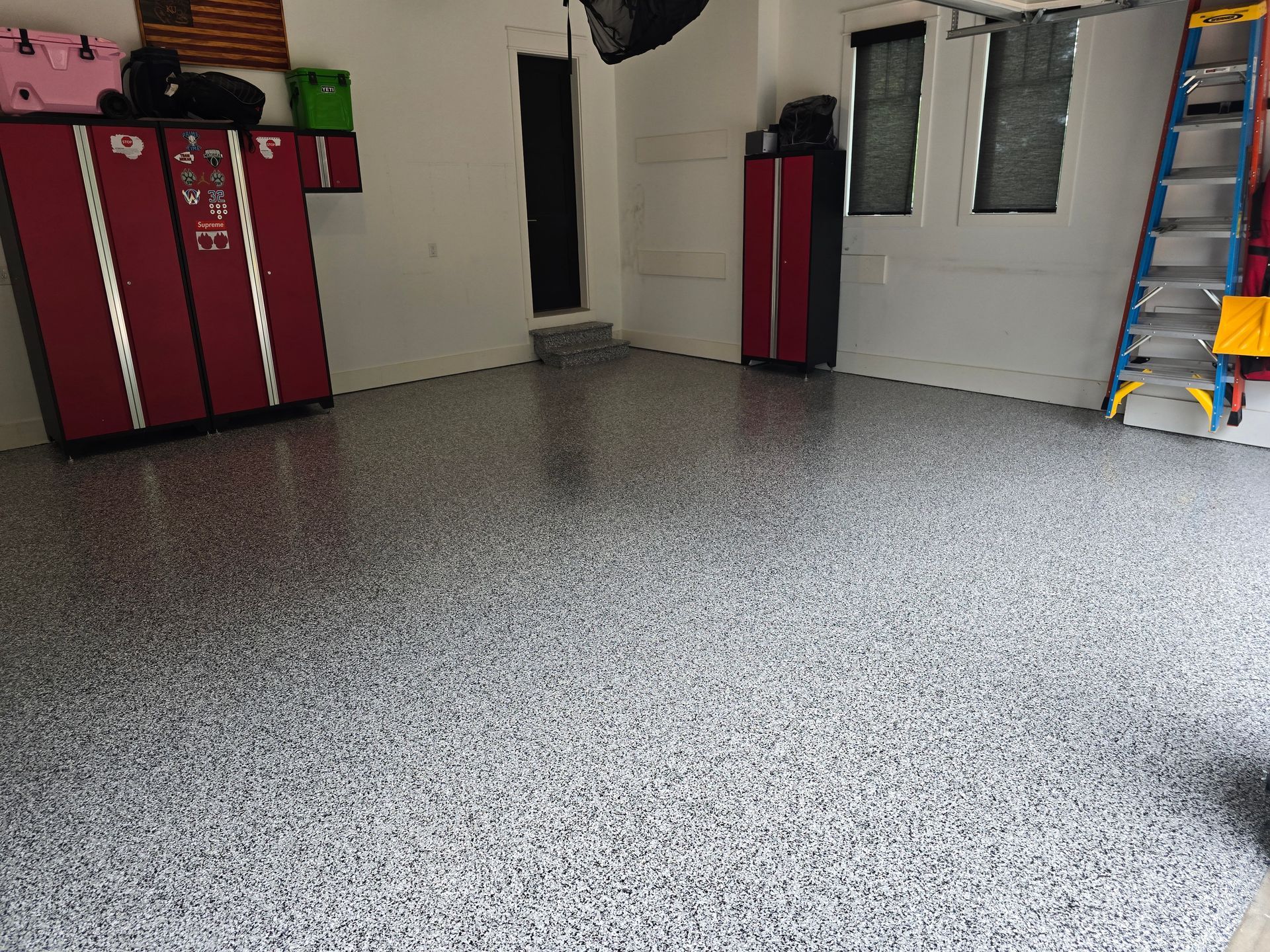 A garage with a gray floor and red cabinets and a ladder.