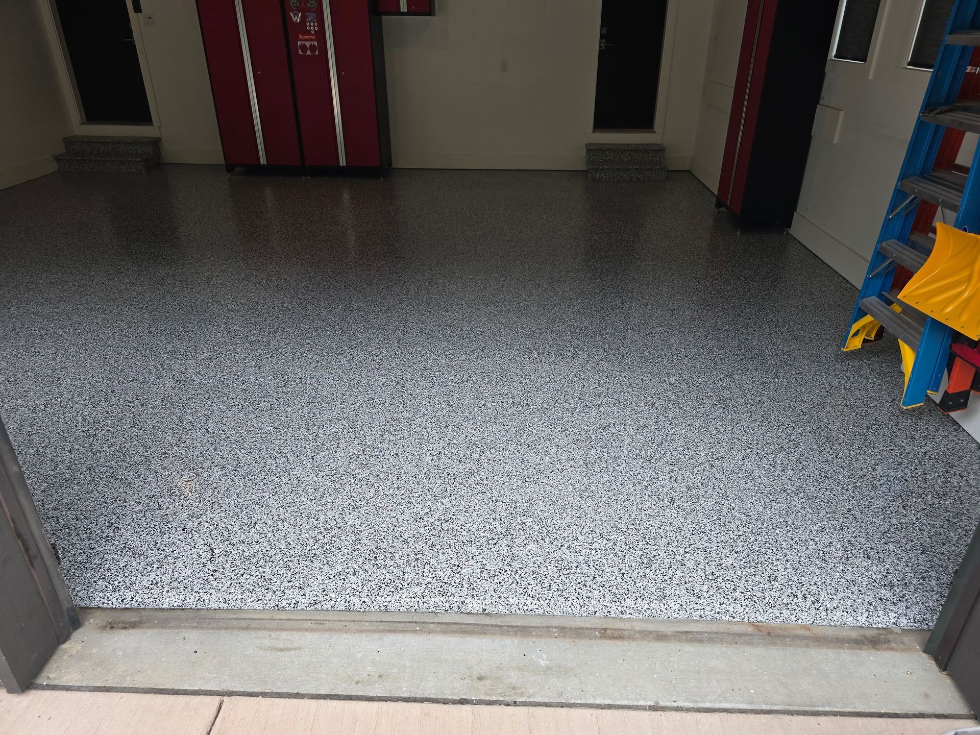 A garage with a ladder and a gray floor.