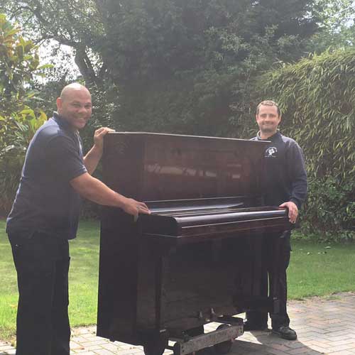 two removal men carrying out an antique piano