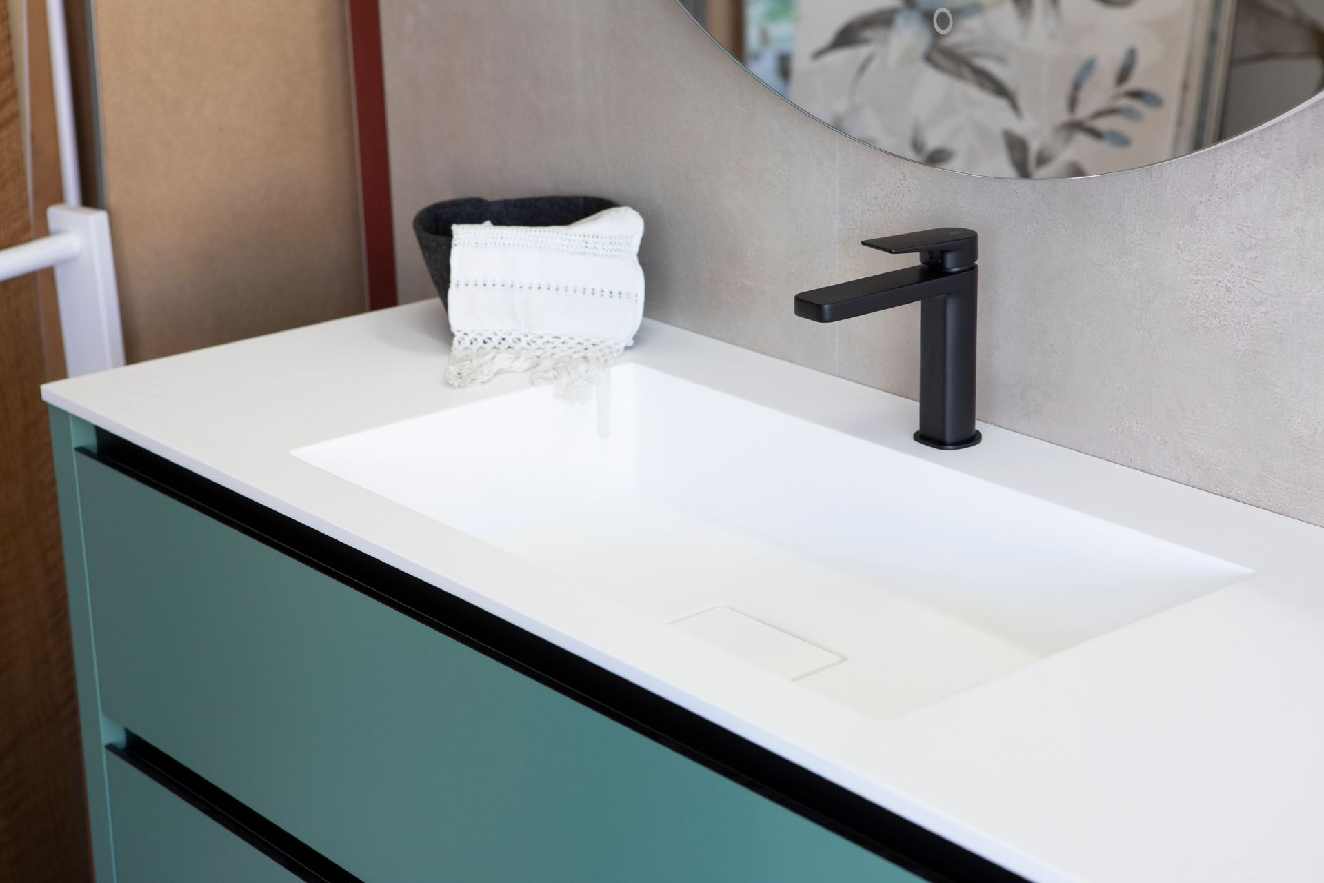 Mobile bagno con lavandino bianco, rubinetto nero e mobiletto verde acqua.